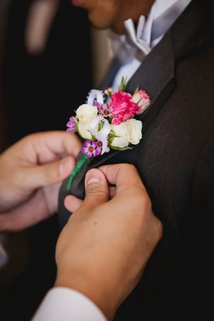 Groomsman pinning a white and pink flower boutonniere onto the groom's jacket