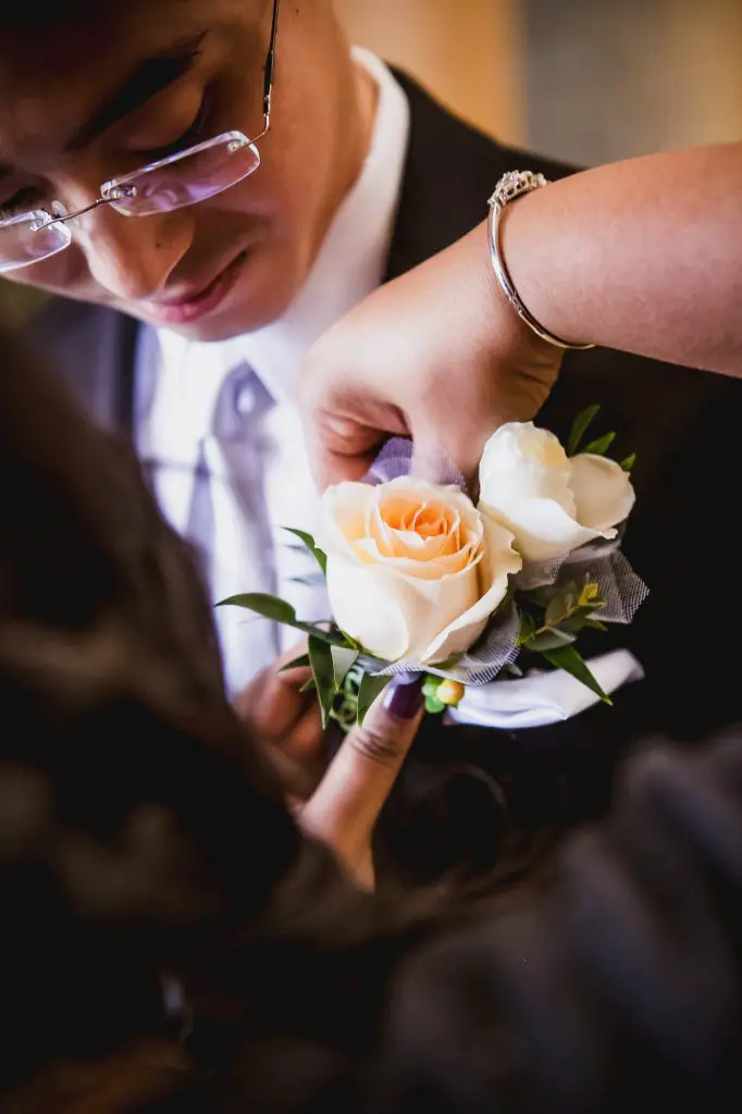 Woman pinning an orange rose boutonniere on the groom's lapel on the wedding day