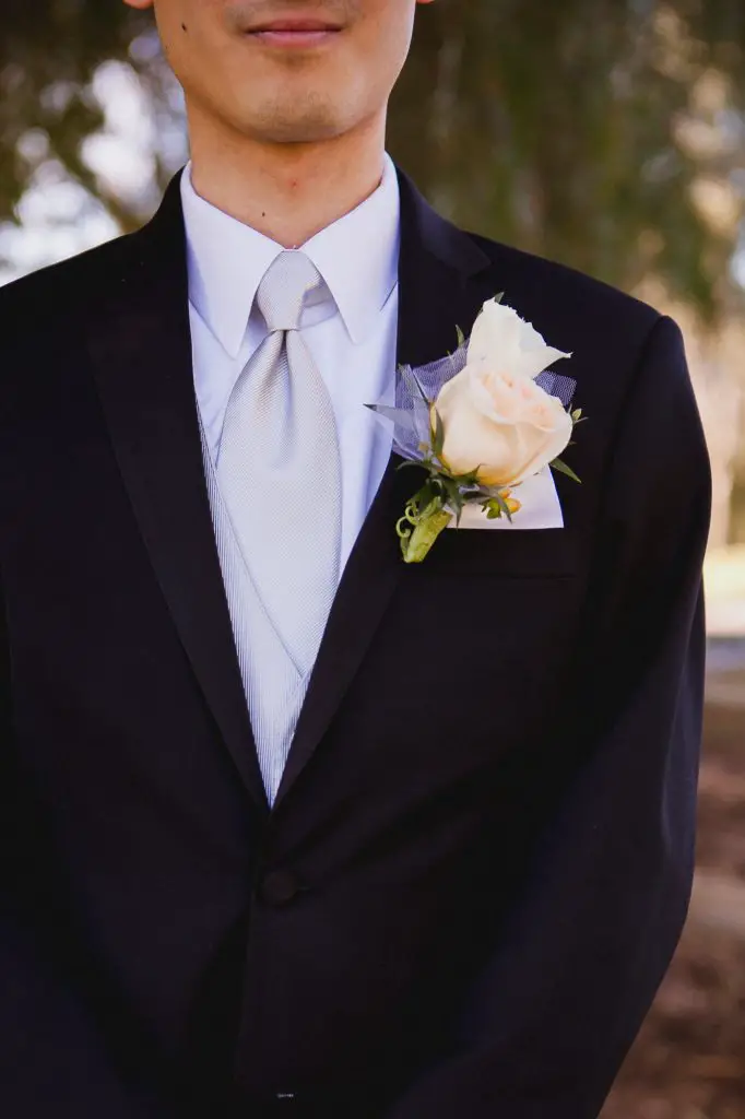 Detail photo of the groom's rose boutonniere and light gray tie
