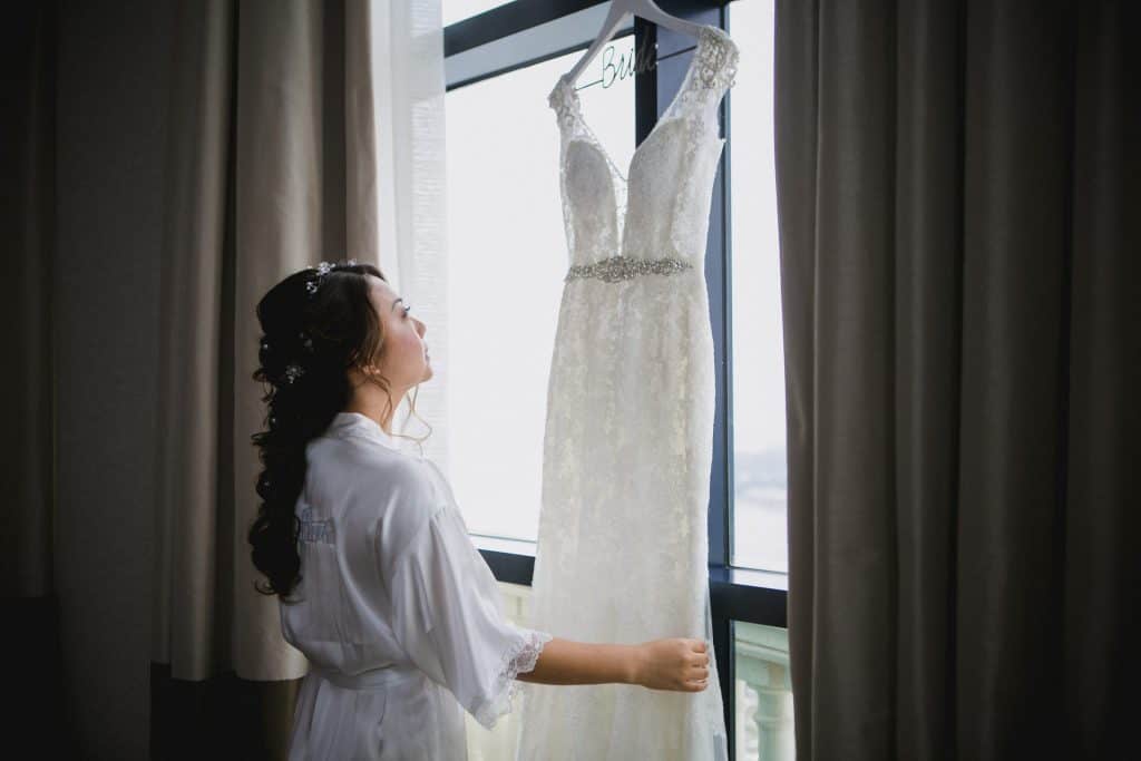 Bride looking at her wedding gown hanging on a hotel window