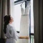 Bride looking at her wedding gown hanging on a hotel window