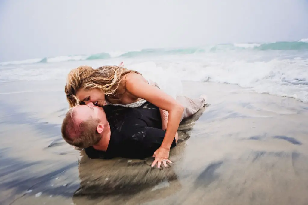 Couple kissing in the beach sands while wearing their wedding suit and dress